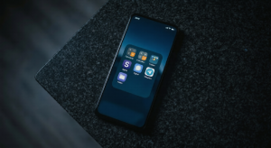 A top-down shot of a smartphone in the dark, its screen glowing and displaying icons for disguised 'vault apps' (calculator icons) and encrypted messengers (Signal/Telegram style icons).